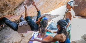 woman bouldering while another women is supporting her and man watches out from distance