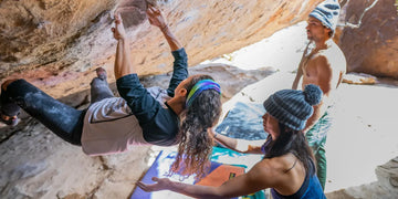 woman bouldering while another women is supporting her and man watches out from distance