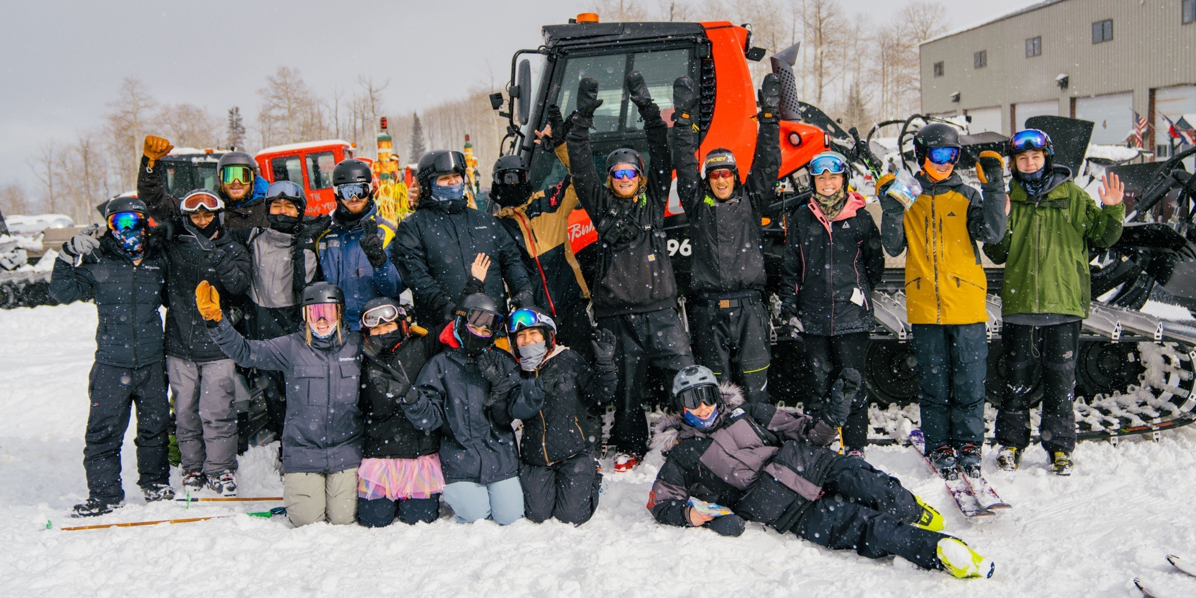 group of people in snowboard and ski gear standing at base of mountain posing for camera